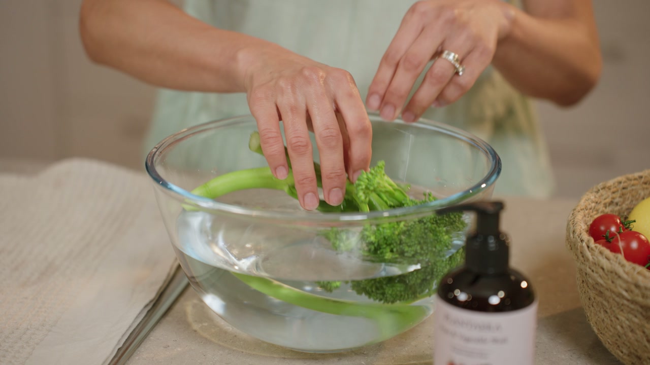 Hands adding fresh greens into a bowl of water